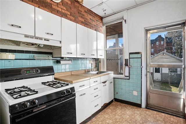 kitchen with range with gas cooktop, light countertops, white cabinetry, a sink, and under cabinet range hood