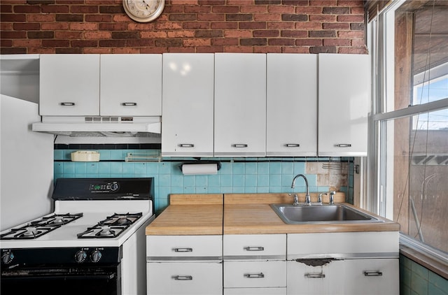 kitchen featuring white cabinets, a sink, under cabinet range hood, and gas range oven