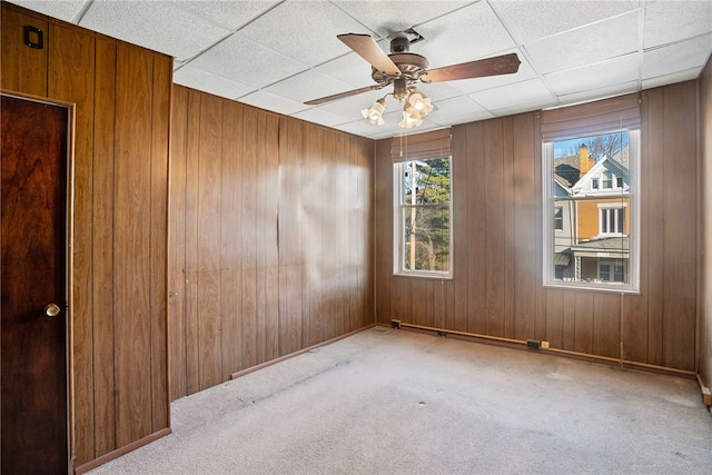 spare room with a paneled ceiling, carpet flooring, and wood walls