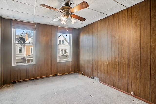 unfurnished room featuring ceiling fan, a drop ceiling, wood walls, carpet flooring, and baseboards