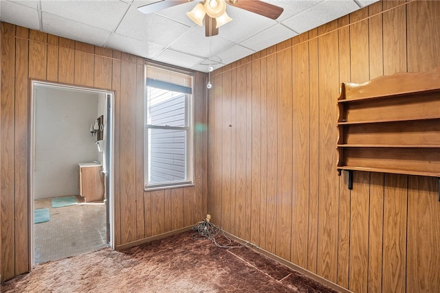 carpeted spare room featuring a ceiling fan, a drop ceiling, and wood walls