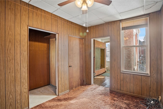 corridor with a paneled ceiling, light colored carpet, and wooden walls