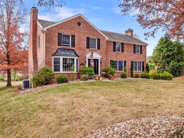 colonial-style house featuring cooling unit, brick siding, a chimney, and a front lawn