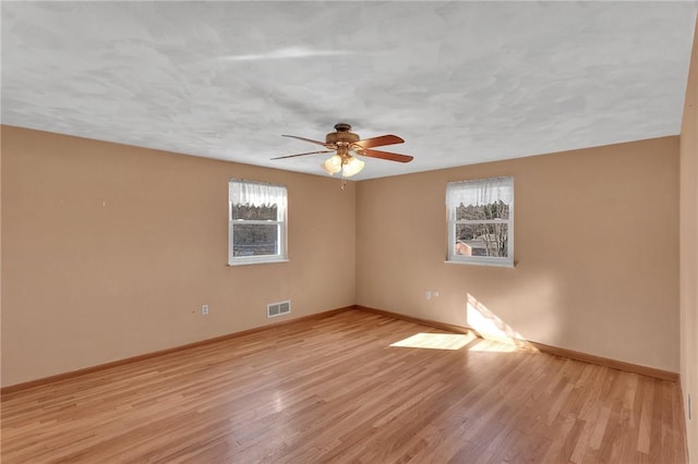 unfurnished room featuring baseboards, a ceiling fan, visible vents, and light wood-style floors