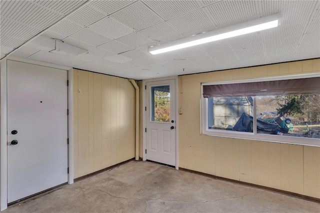 interior space featuring concrete flooring, wooden walls, and baseboards