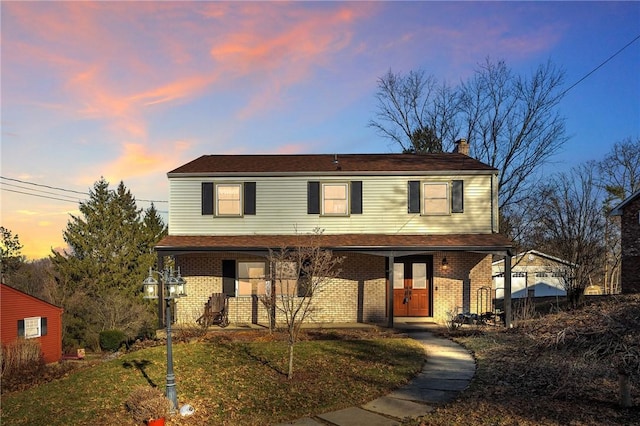 view of front facade featuring a front yard, covered porch, brick siding, and a chimney