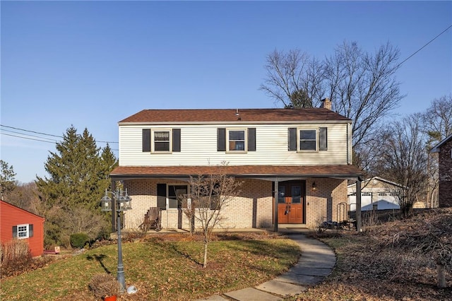 view of front of property with a porch, a front yard, brick siding, and a chimney