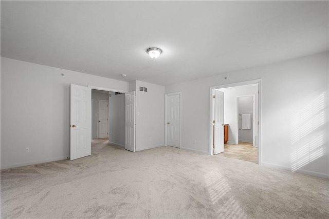 unfurnished bedroom with light colored carpet, visible vents, baseboards, and ensuite bathroom