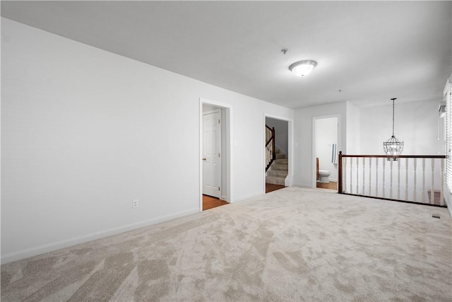 carpeted empty room with baseboards, stairs, and an inviting chandelier