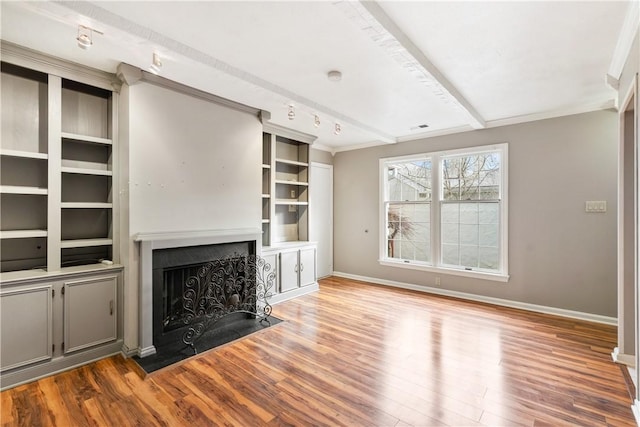 unfurnished living room with a fireplace with flush hearth, beamed ceiling, baseboards, and wood finished floors