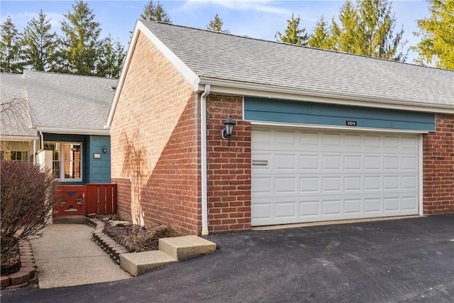 exterior space featuring aphalt driveway, brick siding, and a shingled roof