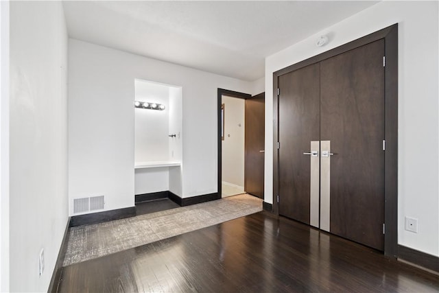 unfurnished bedroom with a closet, wood finished floors, visible vents, and baseboards