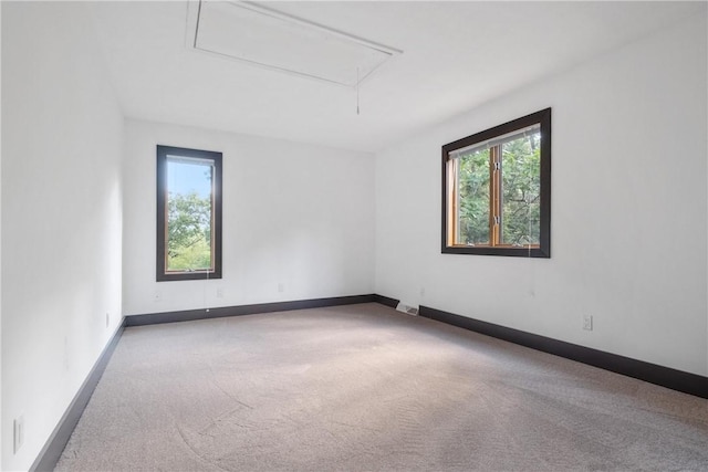 carpeted spare room featuring plenty of natural light, attic access, and baseboards