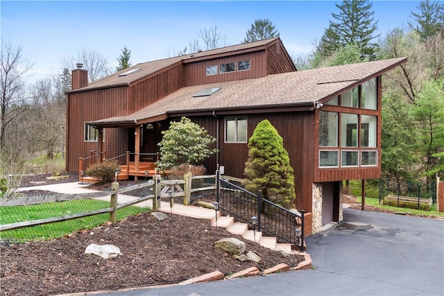 rustic home featuring roof with shingles, driveway, and a chimney