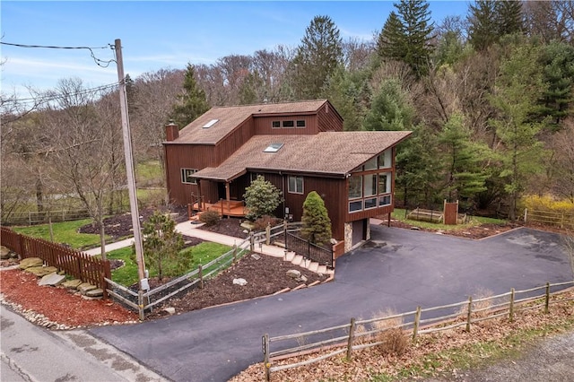 rustic home with a wooded view, aphalt driveway, and fence