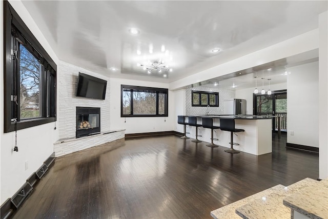 living area featuring dark wood-style floors, a stone fireplace, and baseboards