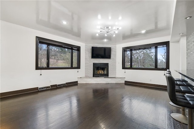 unfurnished living room with a notable chandelier, a large fireplace, visible vents, baseboards, and hardwood / wood-style floors