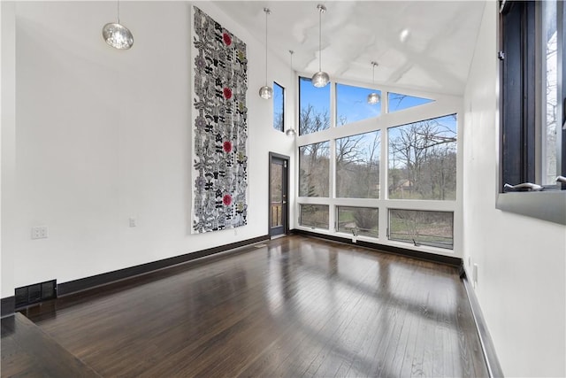 empty room with wood-type flooring, visible vents, a towering ceiling, and baseboards