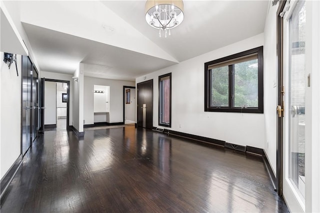 spare room featuring lofted ceiling, baseboards, a chandelier, and wood finished floors