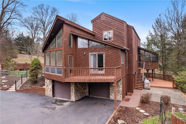 rear view of property featuring a sunroom, stone siding, stairway, an attached garage, and a deck