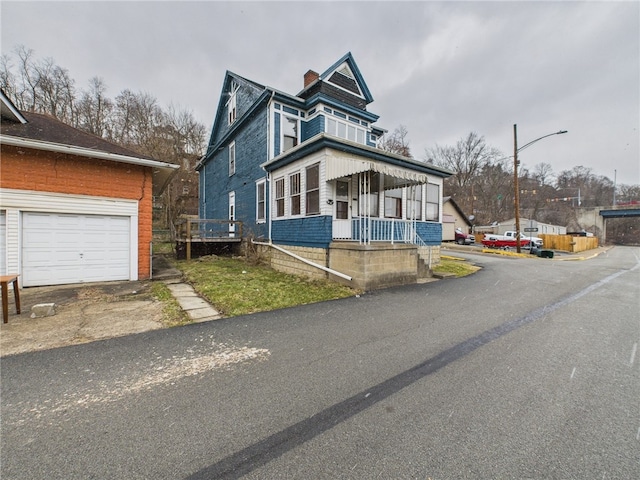 view of front of home featuring covered porch, a chimney, and a garage