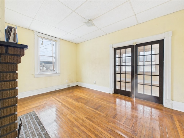 unfurnished living room with a paneled ceiling, french doors, wood-type flooring, and baseboards