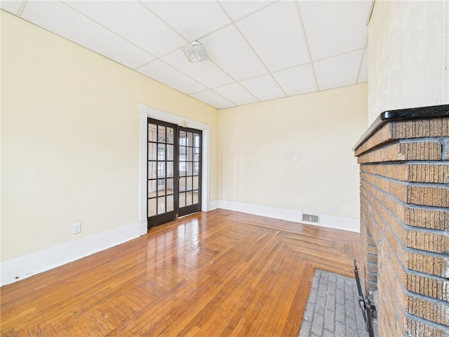 unfurnished living room with baseboards, visible vents, wood-type flooring, french doors, and a paneled ceiling