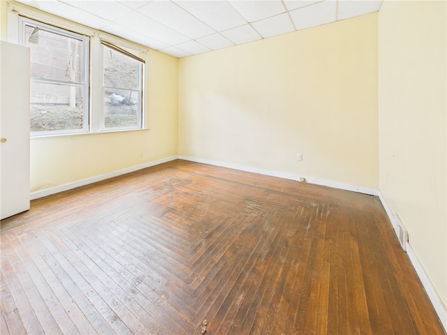 empty room featuring wood-type flooring, baseboards, and a drop ceiling