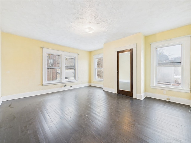 empty room with dark wood-style floors, a textured ceiling, and baseboards