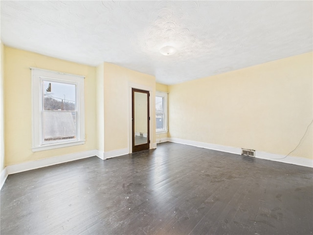 spare room with dark wood-type flooring, visible vents, a textured ceiling, and baseboards