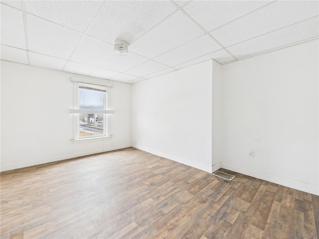 spare room featuring a paneled ceiling, baseboards, visible vents, and wood finished floors