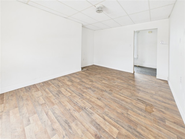 empty room featuring a drop ceiling, baseboards, and wood finished floors