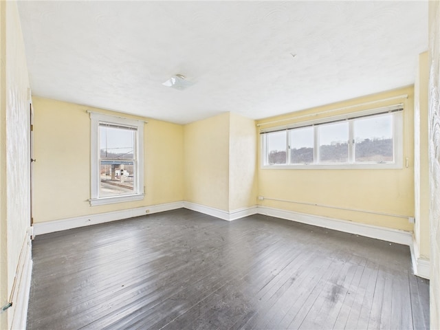 spare room featuring dark wood-type flooring, a healthy amount of sunlight, and baseboards
