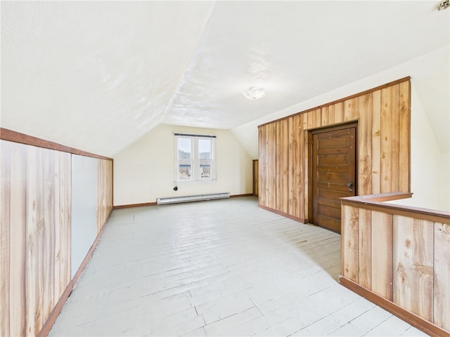 additional living space with a baseboard heating unit, lofted ceiling, and light wood-style flooring