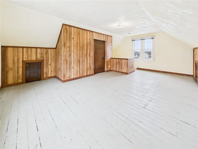 bonus room featuring lofted ceiling, light wood-style flooring, and wooden walls