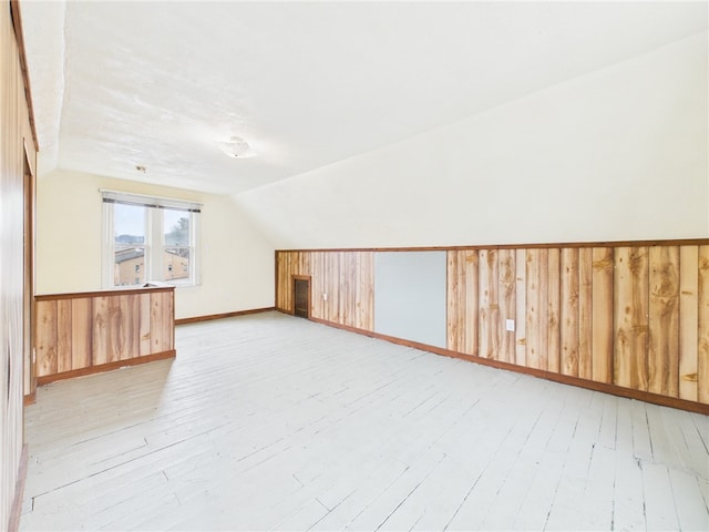 additional living space with lofted ceiling, wainscoting, wooden walls, and light wood finished floors