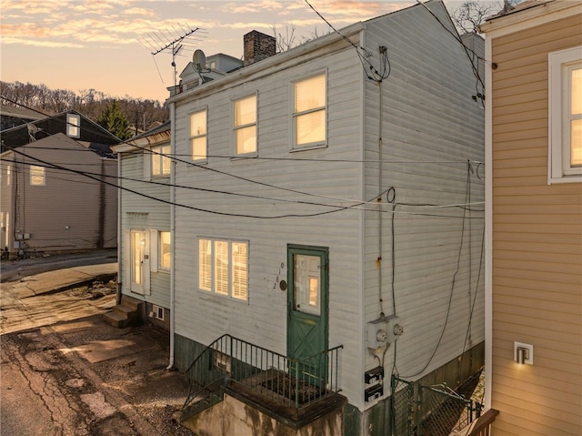 back of house at dusk with entry steps and a chimney