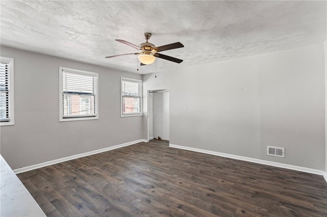 unfurnished room featuring dark wood-style floors, visible vents, a textured ceiling, and baseboards