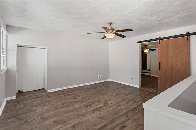 interior space featuring a barn door, visible vents, dark wood finished floors, ceiling fan, and a textured ceiling