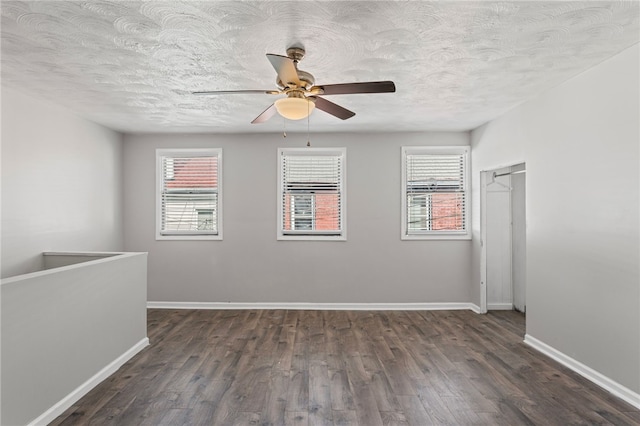 empty room with dark wood-style floors, a textured ceiling, a ceiling fan, and baseboards