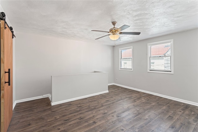 spare room with dark wood-style floors, a barn door, baseboards, and a textured ceiling