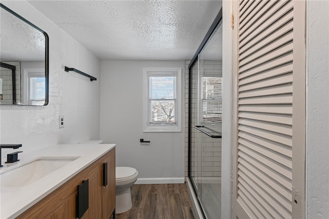 full bath featuring a stall shower, a textured ceiling, toilet, and wood finished floors