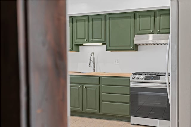 kitchen featuring range hood, freestanding refrigerator, stainless steel range with gas stovetop, a sink, and green cabinetry