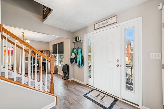 foyer entrance with baseboards, stairway, wood finished floors, a textured ceiling, and a notable chandelier