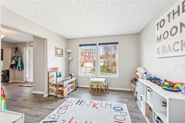 recreation room with a textured ceiling, baseboards, and wood finished floors