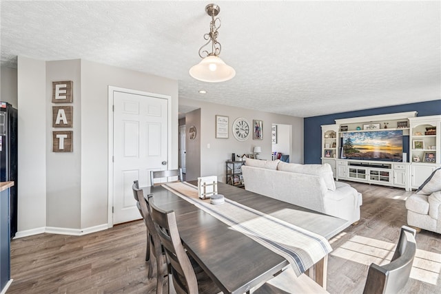 dining area with a textured ceiling, baseboards, and wood finished floors