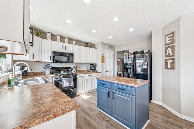 kitchen featuring a center island, light wood-type flooring, black appliances, white cabinetry, and a sink