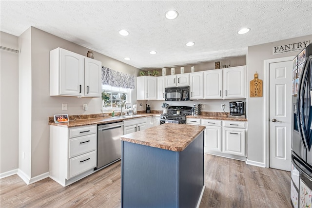 kitchen with appliances with stainless steel finishes, white cabinetry, a sink, and light wood-style flooring