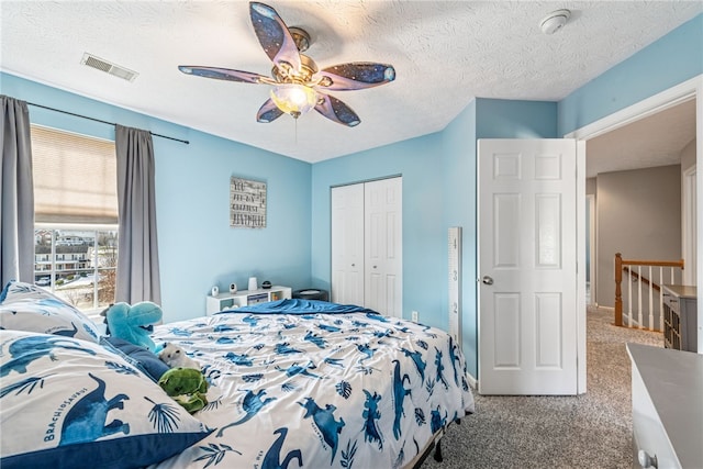 carpeted bedroom featuring a closet, visible vents, ceiling fan, and a textured ceiling