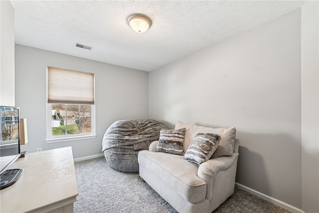 living area featuring a textured ceiling, carpet, visible vents, and baseboards